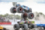 Eye-level view of a monster truck mid-air while jumping over another monster truck